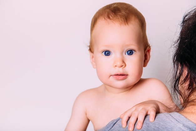 Il ritratto di un piccolo bambino sveglio fa capolino nella sorpresa e nella gioia sopra la sua spalla della madre. Il concetto di cura e infanzia. Isolato su uno sfondo bianco.