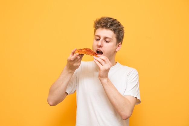 Il ritratto di un ragazzo in una maglietta bianca tiene un pezzo di pizza nelle sue mani