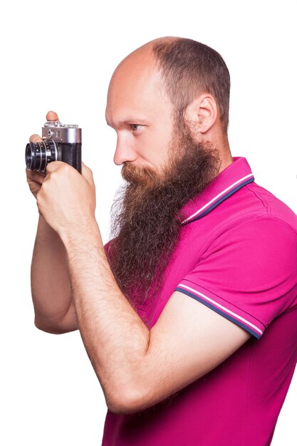 Il ritratto di un uomo calvo e barbuto fotografo con una maglietta rosa che tiene in mano una macchina fotografica classica. isolato su sfondo bianco. girato in studio.