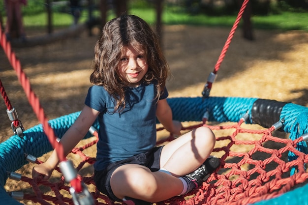 Il ritratto di una bella ragazza caucasica si siede su un'altalena rotonda di corda nel parco del parco giochi