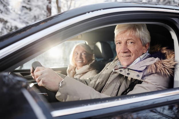 Il ritratto di una coppia senior allegra che guida l'auto in inverno si concentra sull'uomo anziano al volante che guarda