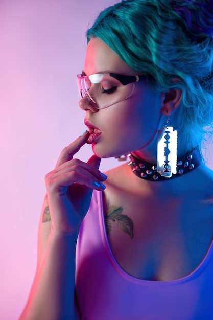 Il ritratto di una donna brillante con i capelli blu in occhiali trasparenti alla luce al neon