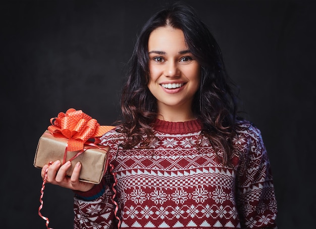 Il ritratto di una donna bruna sorridente festosa con lunghi capelli ricci, vestita con un maglione rosso, tiene i regali di Natale.