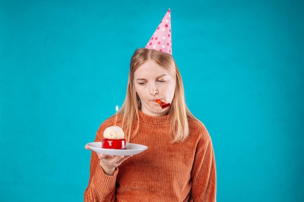 Il ritratto di una donna degli anni '20 ha un'espressione del viso insoddisfatta indossa abiti festivi festeggia il compleanno tiene una gustosa torta isolata su sfondo blu