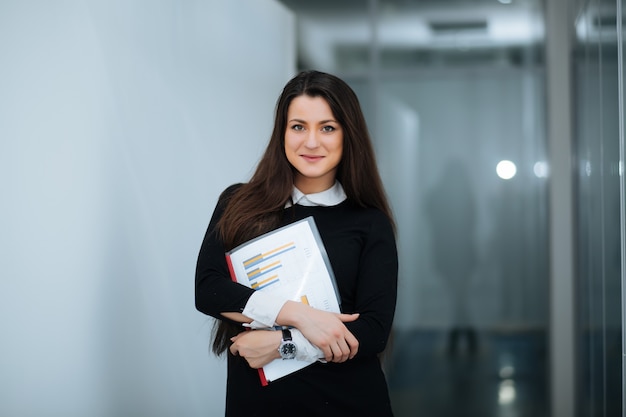 Il ritratto di una femmina casuale che sta con le armi ha attraversato ad un ufficio luminoso