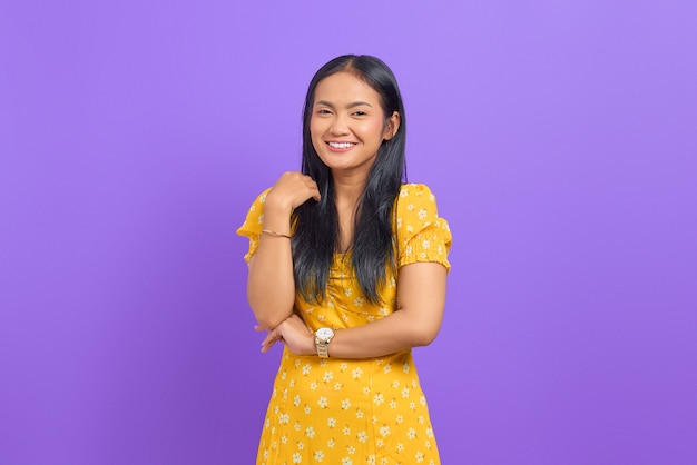Il ritratto di una giovane donna asiatica sorridente ha alzato la mano con un braccio incrociato su sfondo viola