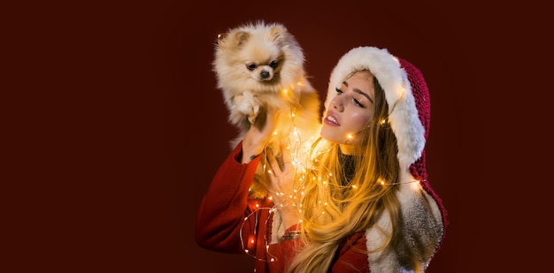 Il ritratto di una giovane donna celebra le vacanze di natale invernali tiene il cucciolo di cane su sfondo rosso