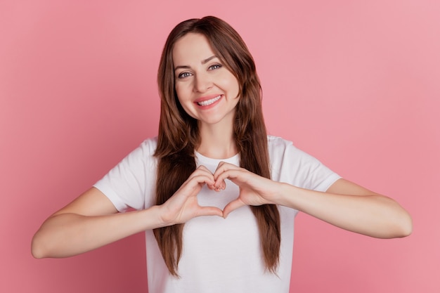 Il ritratto di una ragazza allegra e piuttosto affettuosa mostra un sorriso a trentadue denti con il simbolo del cuore su sfondo rosa