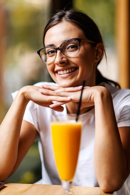 Il ritratto di una ragazza felice si siede in un bar con le mani sotto il mento e guarda la telecamera