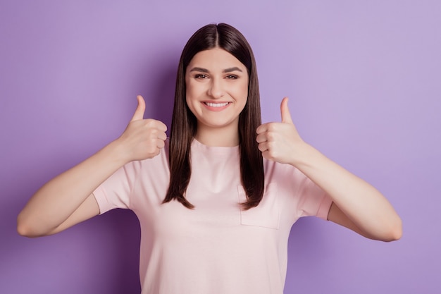 Il ritratto di una signora affascinante e affidabile alza il pollice in su con un sorriso splendente e guarda la telecamera su sfondo viola