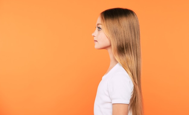 Il ritratto di vista laterale di bella piccola ragazza bionda in maglietta bianca sta posando isolato su fondo giallo