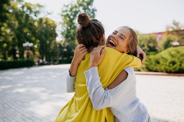 Il ritratto emotivo all'aperto di due adorabili ragazze sta abbracciando e ridendo nel parco in una calda giornata di sole