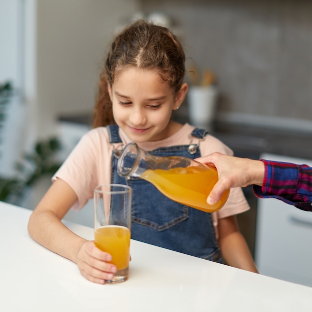 Il ritratto frontale del primo piano di una mano versa il succo d'arancia della bambina sveglia per la prima colazione.