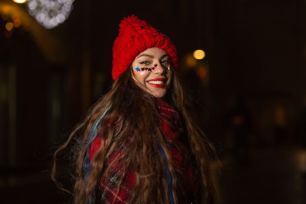 Il ritratto invernale di una donna allegra con i capelli lunghi indossa un cappello rosso che si diverte per strada