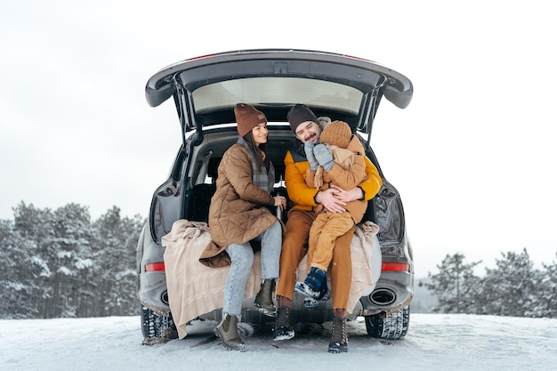 Il ritratto invernale di una famiglia si siede sul bagagliaio dell'auto per godersi la vacanza nella foresta