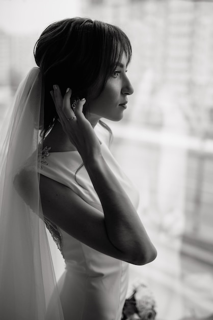 Il ritratto verticale del primo piano di una sposa alla moda, sposa raddrizza il suo ricciolo con la sua mano, foto di profilo. Foto di matrimonio classica. Chiave di basso.