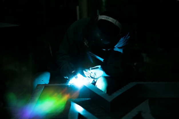 Il saldatore ha usato la mola su acciaio in fabbrica con scintille, processo di saldatura presso l'officina industriale, mani con strumento nel telaio.