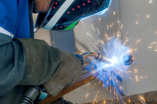 Il saldatore mascherato lavora in officina e le scintille volano Ritratto in primo piano Sfondo industriale Autentico flusso di lavoro