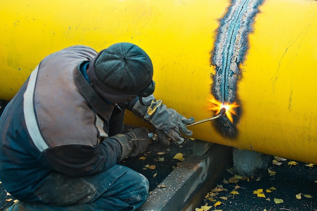 Il saldatore taglia un grande tubo giallo con saldatura ad acetilene per la gassificazione Smaltimento di vecchi tubi metallici usati