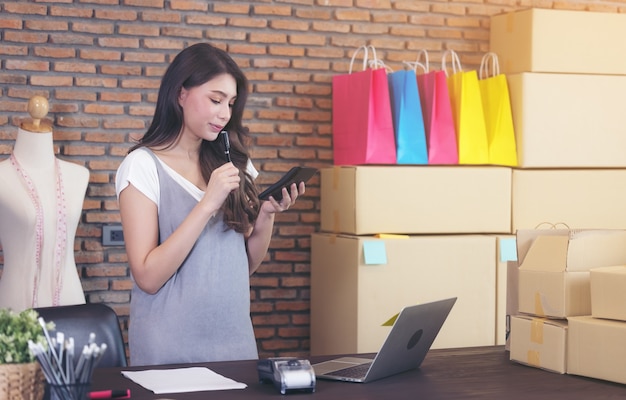 Il sarto della giovane donna con il laptop sta rispondendo ai messaggi di posta elettronica, successo imprenditoriale della donna di affari. Vendita online consegna pacchi