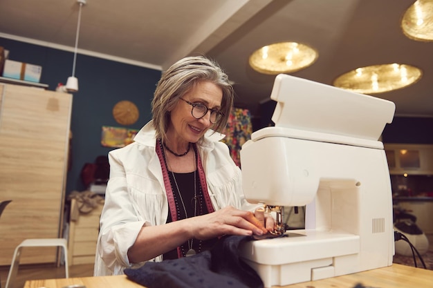 Il sarto elegante del designer di abbigliamento per donna matura cuce i vestiti sulla macchina da cucire cuci il tessuto crea una nuova collezione di vestiti nell'atelier di sartoria