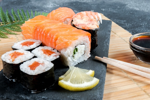 Il sashimi rotola su una lastra di pietra nera. Primo piano di sushi con bacchette e soia