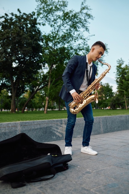 Il sassofonista maschio suona la melodia sul sassofono dorato nel parco estivo, giovane talento. Musicista con sax all'aperto, performance musicale nella natura, interprete jazz