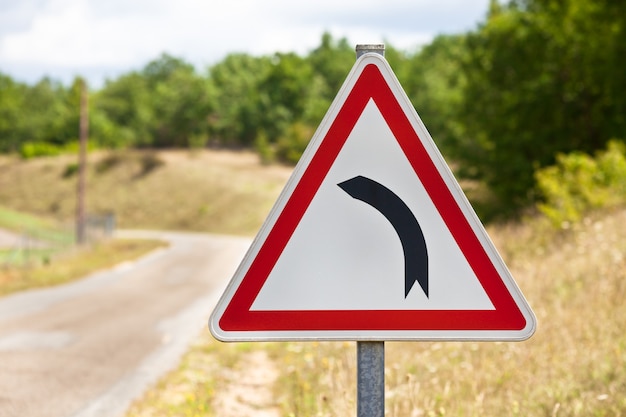 Il segnale stradale triangolare che indica la strada sta girando a sinistra su una strada rurale