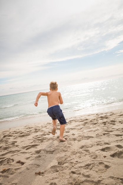 Il simpatico bambino corre rapidamente nell'oceano sulla spiaggia sabbiosa in una mattina di sole