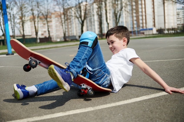 Il simpatico ragazzino è scivolato ed è caduto dallo skateboard sull'asfalto del parco giochi
