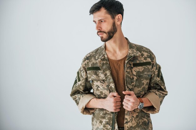 Il soldato in uniforme è in piedi al chiuso contro il muro bianco