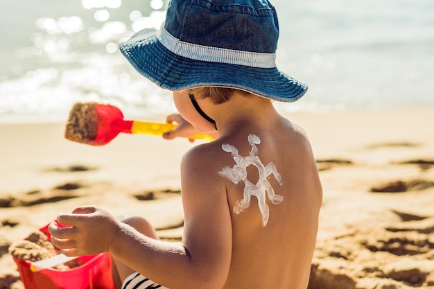 Il sole che disegna crema solare crema solare sulla schiena del neonato bambino caucasico è seduto con la plastica