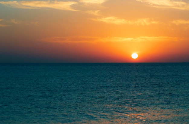 Il sole tramonta sul mare e l'orizzonte è arancione.