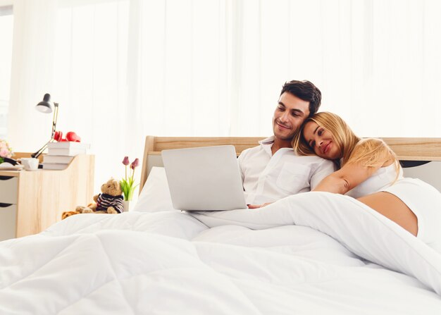 Il sorridere caucasico dell&#39;amante delle coppie gode di di utilizzare il computer portatile insieme sul primo mattino del letto