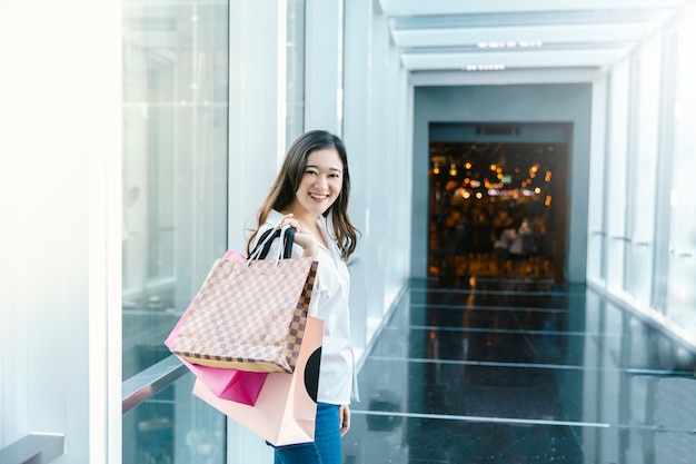 Il sorriso asiatico della donna con i sacchetti della spesa gode nel centro commerciale
