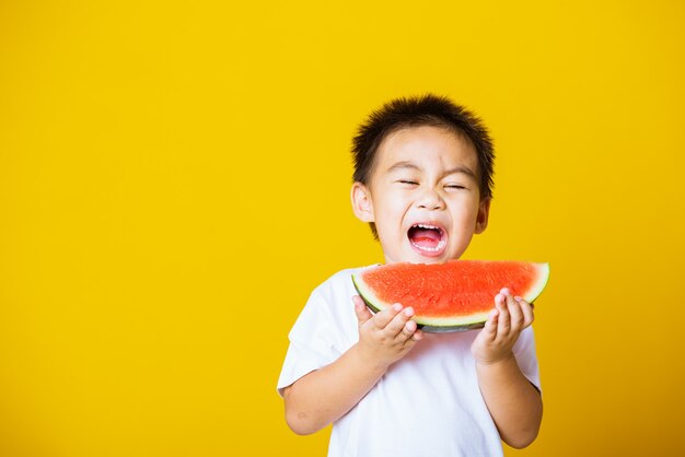 Il sorriso asiatico di risata del ragazzino del bambino tiene l'anguria tagliata fresca per mangiare