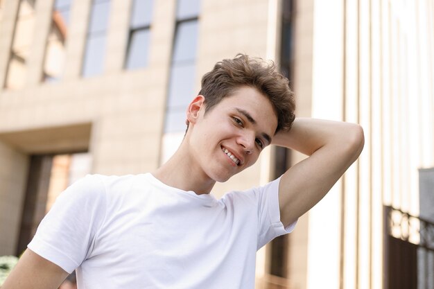 Il sorriso elegante del giovane in una camicia nera alla moda in una t-shirt bianca alla moda in pantaloni neri con un'acconciatura alla moda riposa vicino ad un centro d'affari moderno. ritratto in primo piano