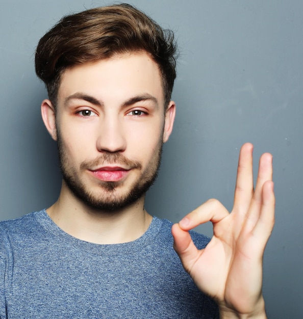 Il sorriso felice dell'uomo bello tiene la mano con il segno giusto di gesto