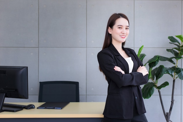 Il successo di una bella donna d'affari asiatica in piedi con le braccia incrociate e sorride felicemente all'ufficio di lavoro