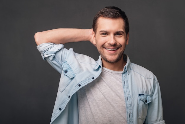 Il suo sorriso è incredibile! Giovane allegro che guarda la telecamera con un sorriso mentre sta in piedi su uno sfondo grigio