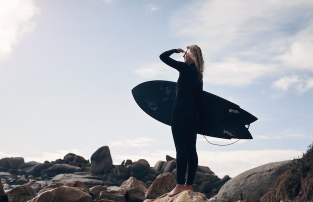 Il surf ci insegna ad essere più pazienti Inquadratura ritagliata di una giovane donna in piedi sulla spiaggia con la sua tavola da surf
