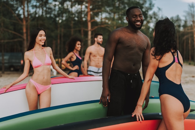 Il surfista afroamericano parla con ragazza sulla spiaggia con il bordo.