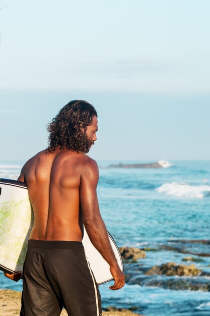 Il surfista tiene in mano una tavola da surf sulla riva dell'Oceano Indiano