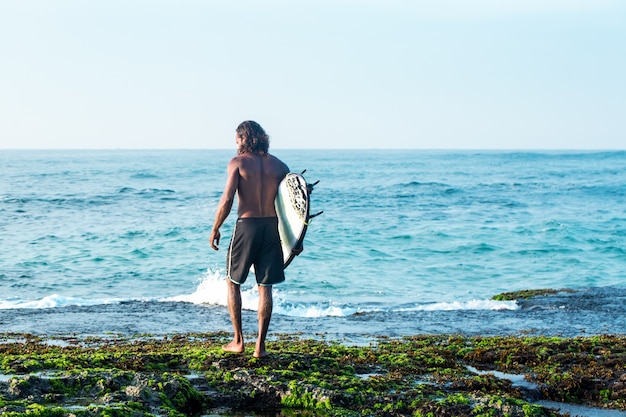 Il surfista tiene in mano una tavola da surf sulla riva dell'Oceano Indiano