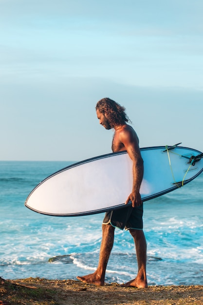 Il surfista tiene in mano una tavola da surf sulla riva dell'Oceano Indiano