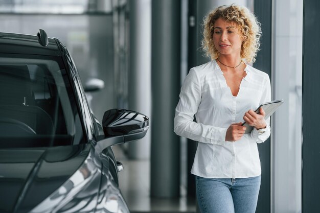 Il tablet è nelle mani La donna con i capelli biondi ricci è in autosalon