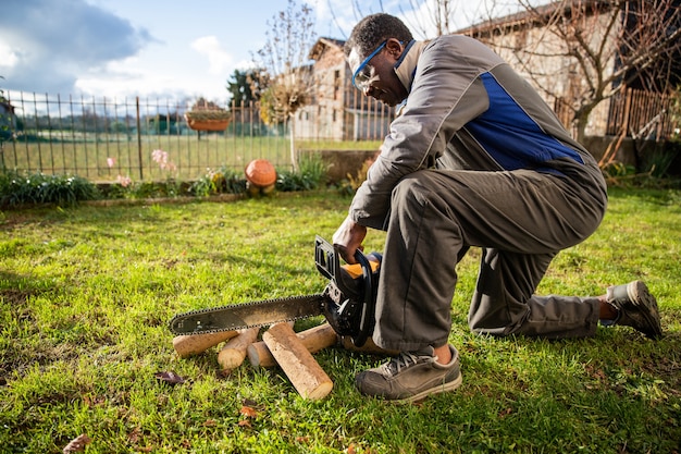 Il taglialegna africano in ginocchio taglia un pezzo di legno con la sua motosega