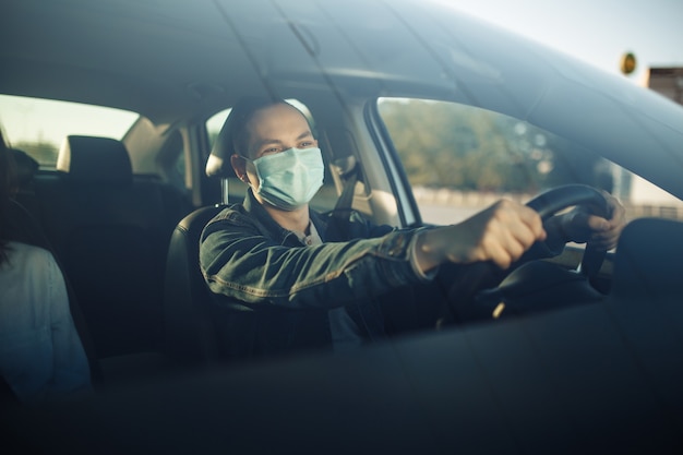 Il tassista che indossa una mascherina medica sterile tiene le mani sul volante.
