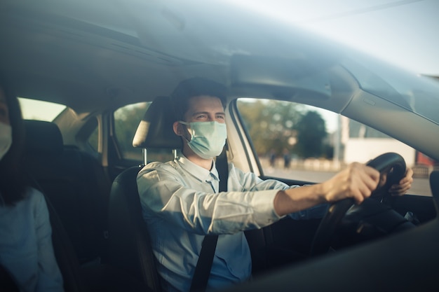 Il tassista del giovane ragazzo tiene le mani sul volante e indossa una mascherina medica sterile.