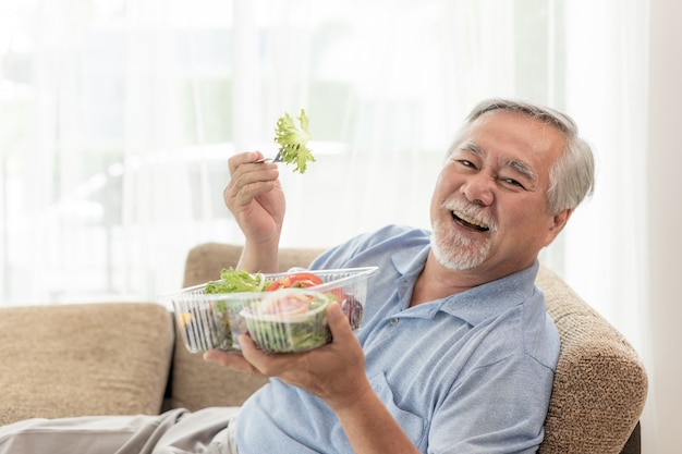 Il tatto dell&#39;uomo senior di stile di vita felice gode di di mangiare l&#39;insalata fresca dell&#39;alimento di dieta sul sofà